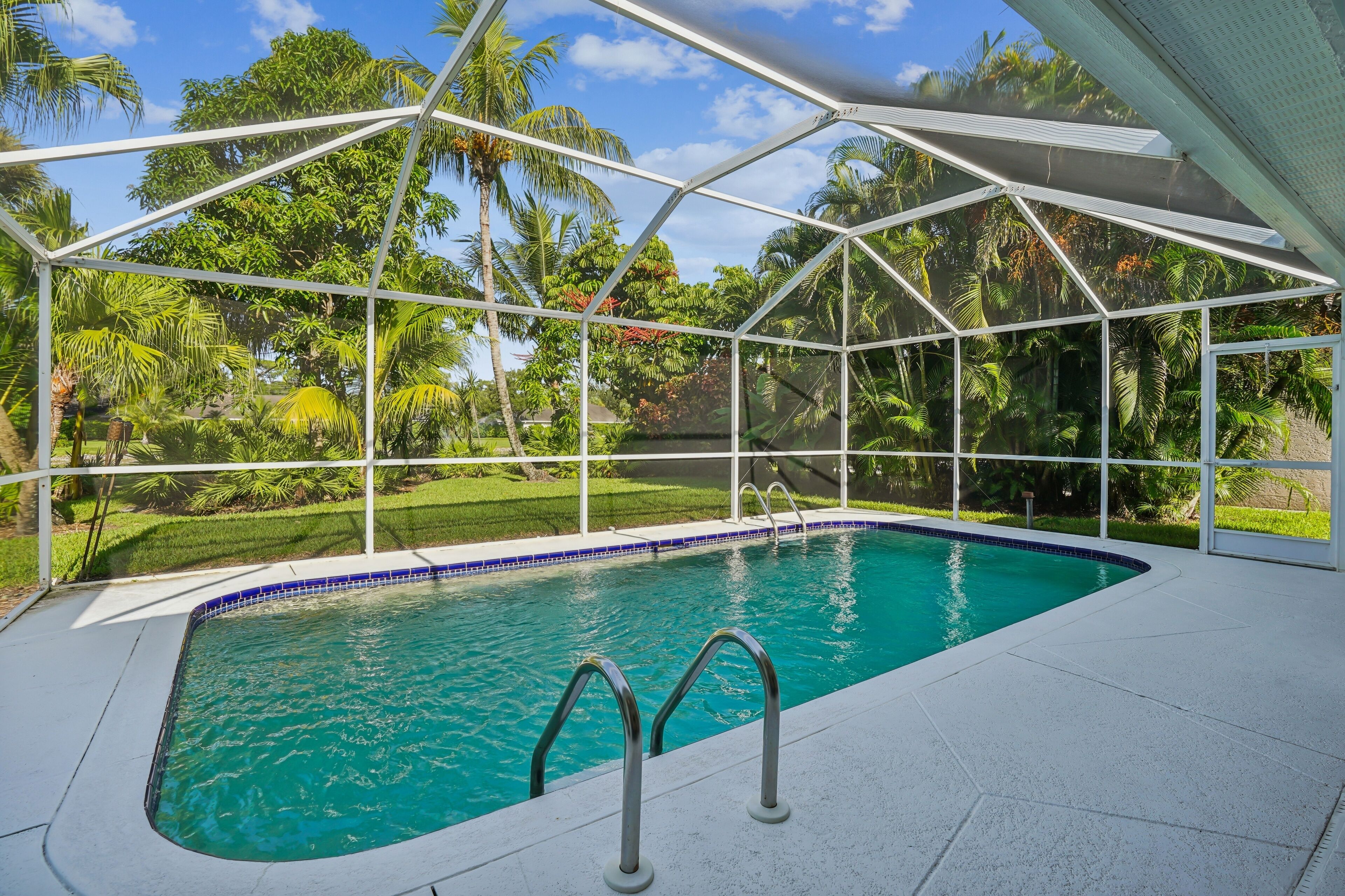 A swimming pool with a glass enclosure, surrounded by lush greenery and palm trees.