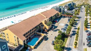 A hotel with a swimming pool, adjacent to a beach with umbrellas and people. - Coral Reef Club 36 3 Bedroom Condo (Destin)
