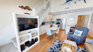A modern living space with a TV, entertainment system, dining area, kitchen, and staircase. - Coral Reef Club 36 3 Bedroom Condo (Destin)