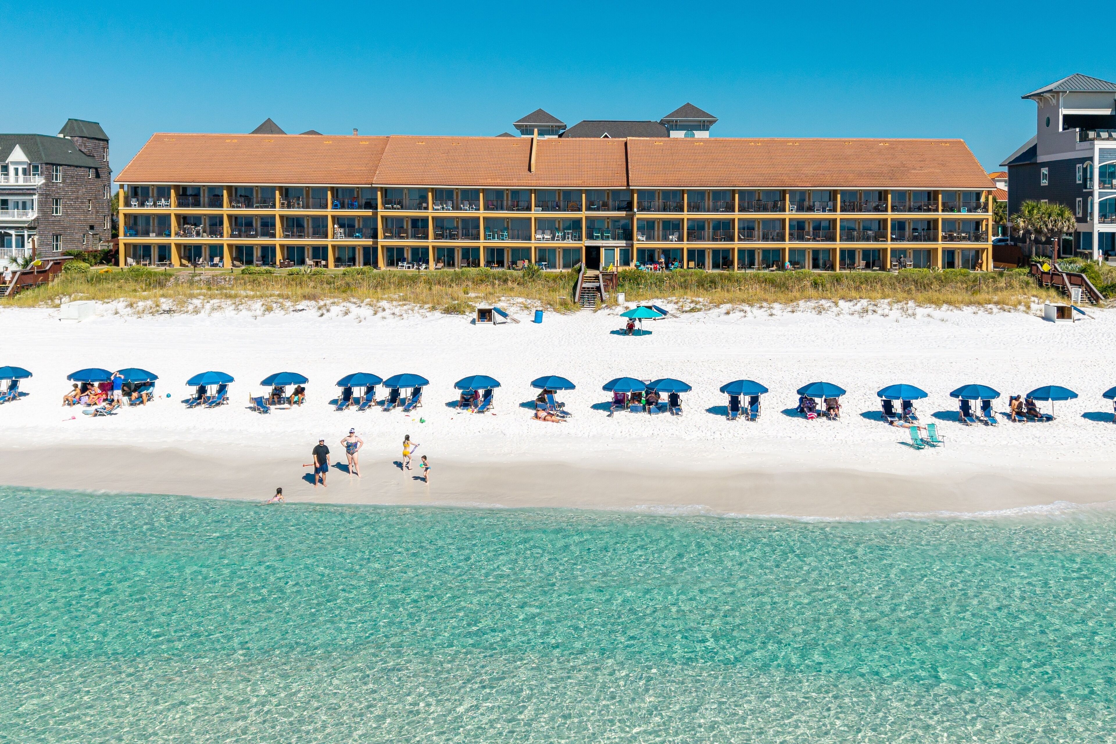 A beachfront hotel with a long building, beach umbrellas, and clear blue water.
