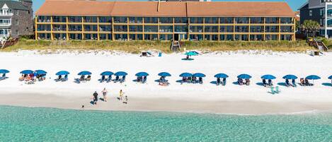A beachfront hotel with a long building, beach umbrellas, and clear blue water.
