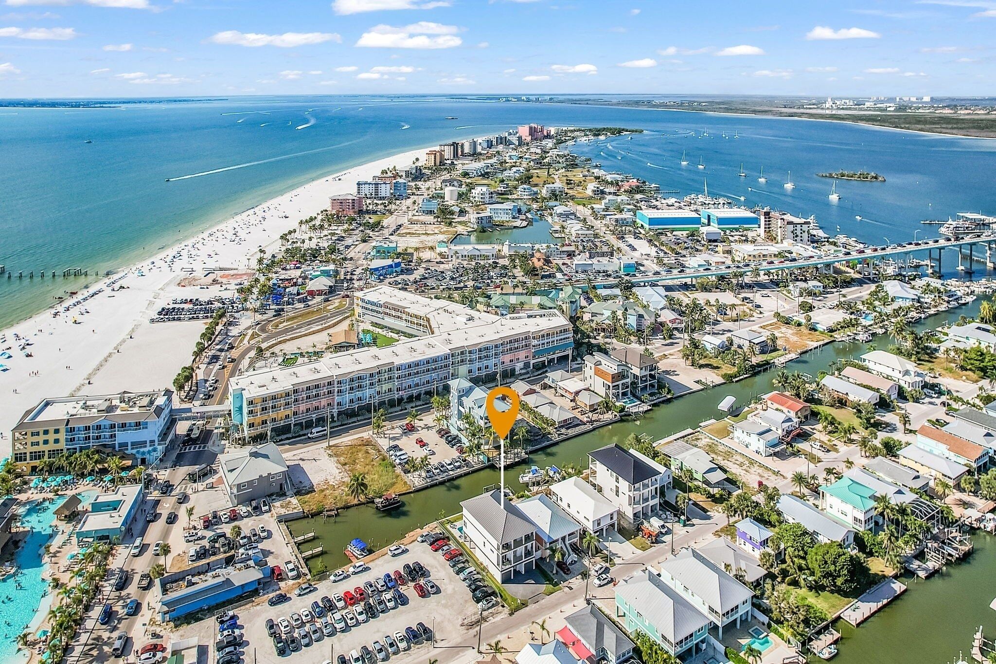 An aerial view of a coastal town with a beach, marina, and various buildings.