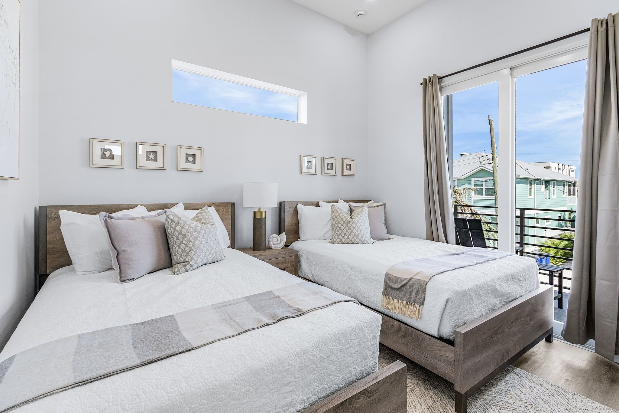 A modern hotel room with two beds, a large window with curtains, and a balcony with a view.