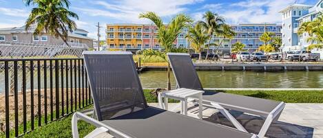A poolside area with lounge chairs and a view of a water body and buildings in the background.