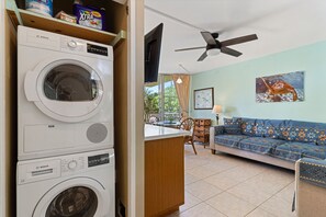 Ein Waschraum mit einer Bosch Waschmaschine, einem Deckenventilator und einem Wohnzimmer inklusive Sofa und Tisch.