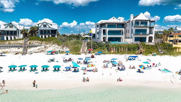A beach resort with multiple beach umbrellas, a sandy beach, and a large building with multiple floors and balconies.