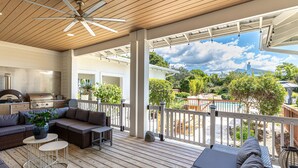 A covered outdoor patio with a grill, seating area, and a view of a backyard.