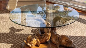 A modern living room with a glass coffee table, beige sofa, and a view of a lake and mountains. - Traverse City Lakefront: Beach, Dock & Hot Tub! (Traverse City)