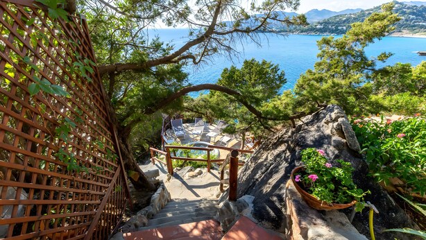 A staircase leading to a terrace with outdoor seating, overlooking a body of water and a mountainous landscape.