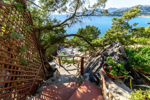 Eine Treppe führt zu einer Terrasse mit Sitzgelegenheiten im Freien, mit Blick auf ein Gewässer und eine Berglandschaft.