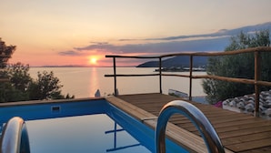 A wooden deck with a pool, overlooking a body of water at sunset.
