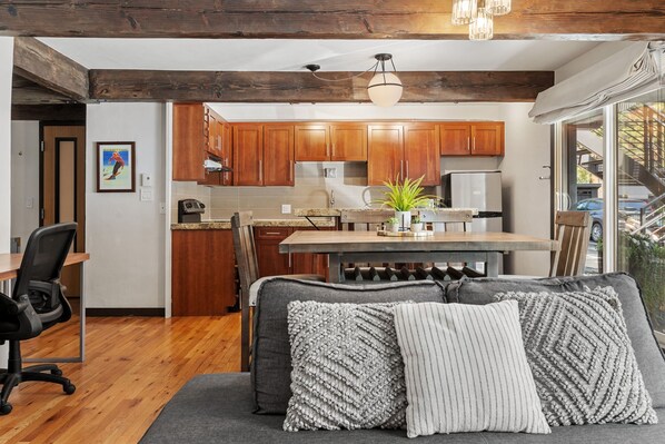 A modern kitchen with wooden cabinets, a dining table, and a sofa with decorative pillows.