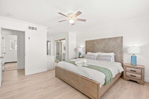 Un dormitorio con cama de madera, paredes blancas, ventilador de techo y mesita de noche con lámpara.