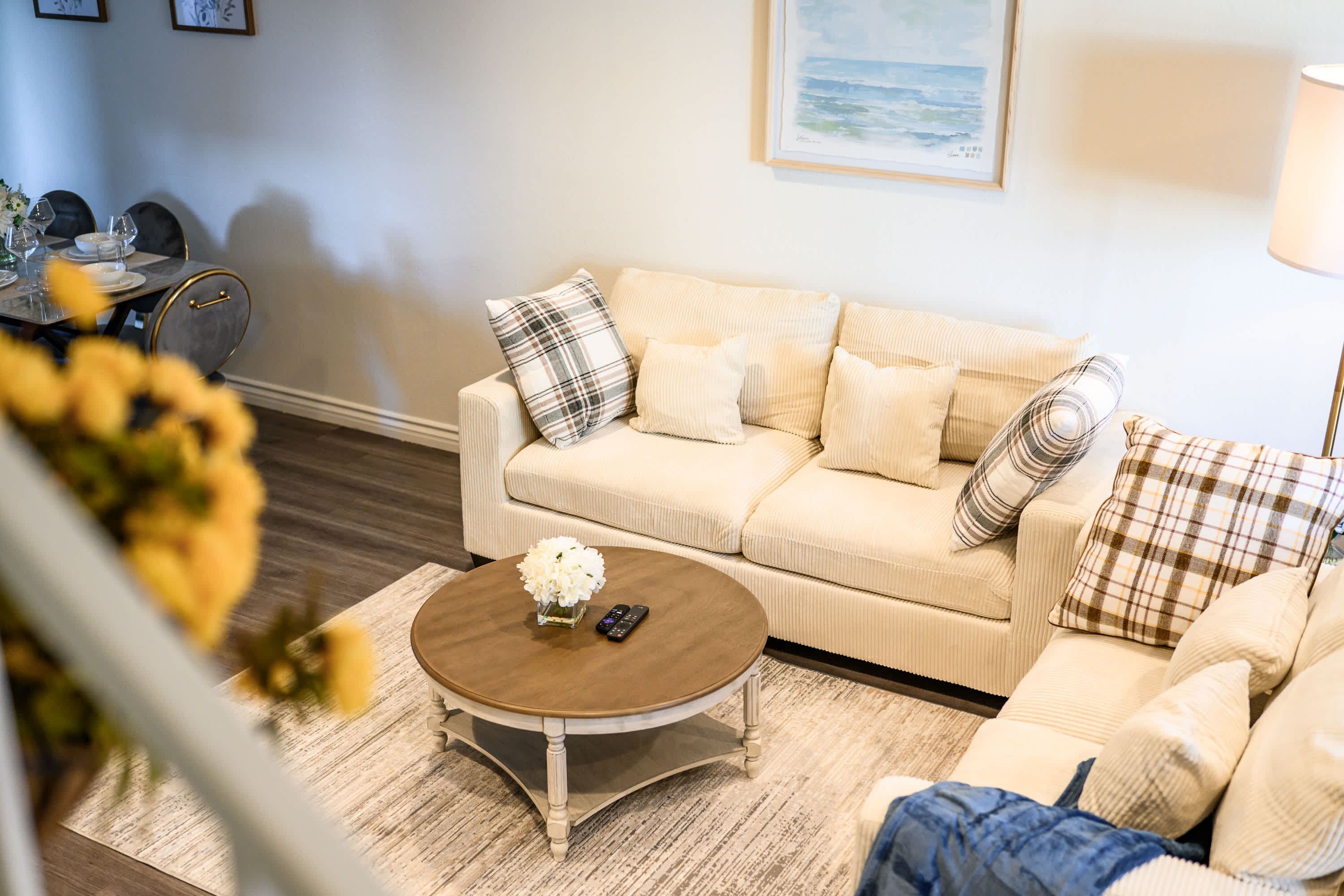 A living room with a beige sofa, a round coffee table, and a dining area with chairs and a table set for a meal.