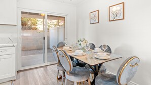 Un comedor con una mesa dispuesta para cuatro, un ventilador de techo y dos cuadros en la pared.