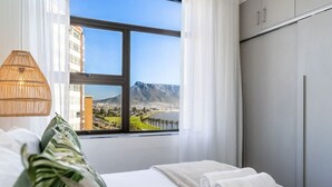 Habitación de hotel con cama, ventana que ofrece vistas a la ciudad y montañas, lámpara y armario.