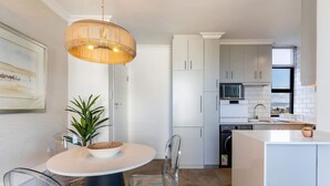 Una cocina moderna con armarios blancos, una mesa redonda de comedor con sillas transparentes y una lámpara colgante.