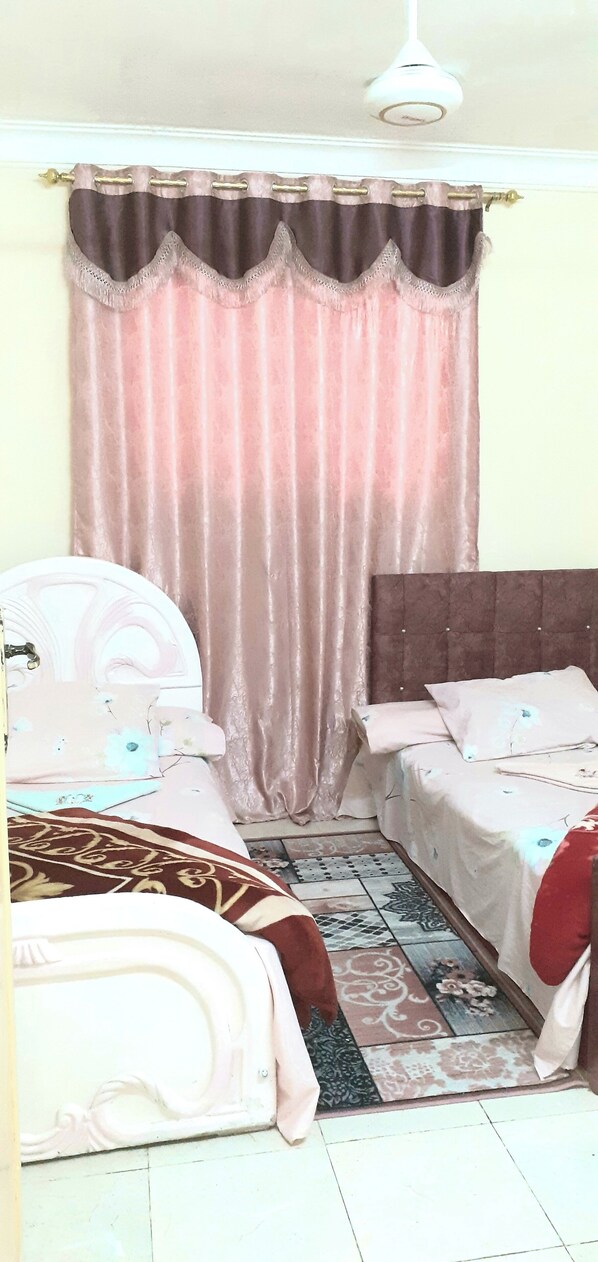 A bedroom with two beds, a patterned rug, and a curtain.