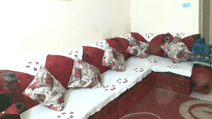 Une rangée de bancs rouges recouverts de tissu, agrémentés de coussins à motifs floraux, une nappe blanche et un panneau encadré accroché au mur.