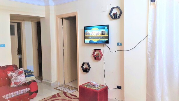 Un salon avec un canapé rouge, un téléviseur fixé au mur et une petite table rouge.