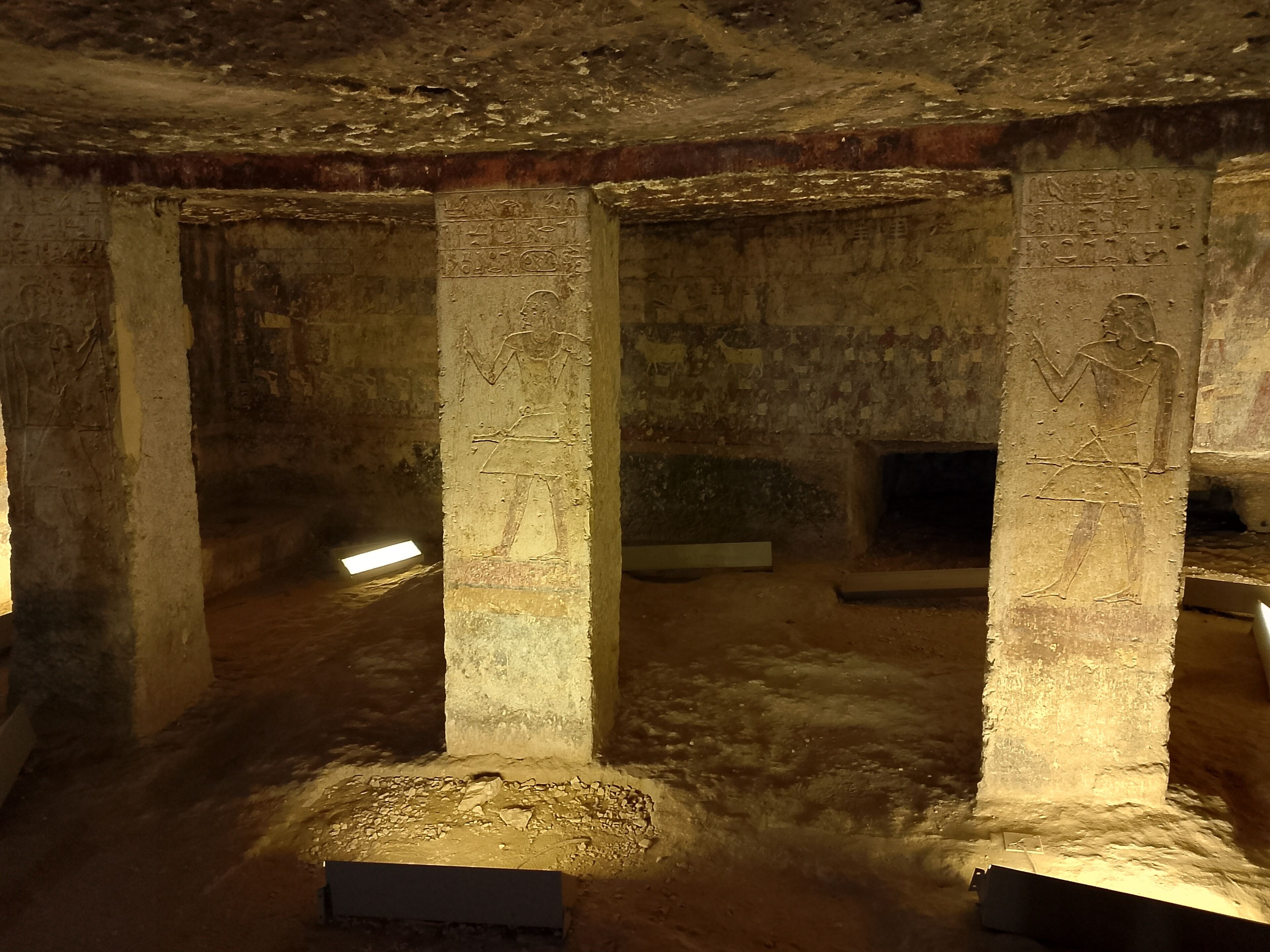 Une pièce ancienne, faiblement éclairée, avec des colonnes de pierre et des sculptures en hiéroglyphes.