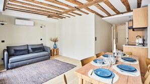 A modern living room with a wooden ceiling, a sofa, a dining table set with blue plates, and a kitchen area with cabinets and a microwave. - Flat Terrace Centre de Paris Bourse (Paris)