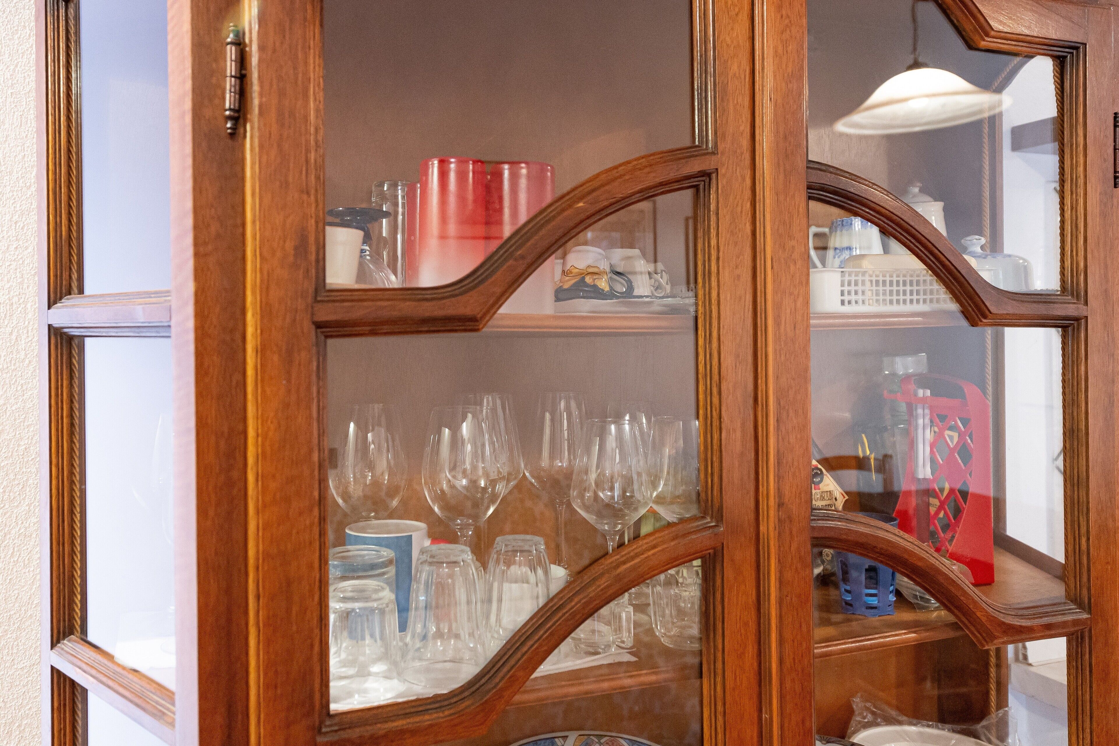 A wooden cabinet with glass doors, containing various glassware and kitchen items.