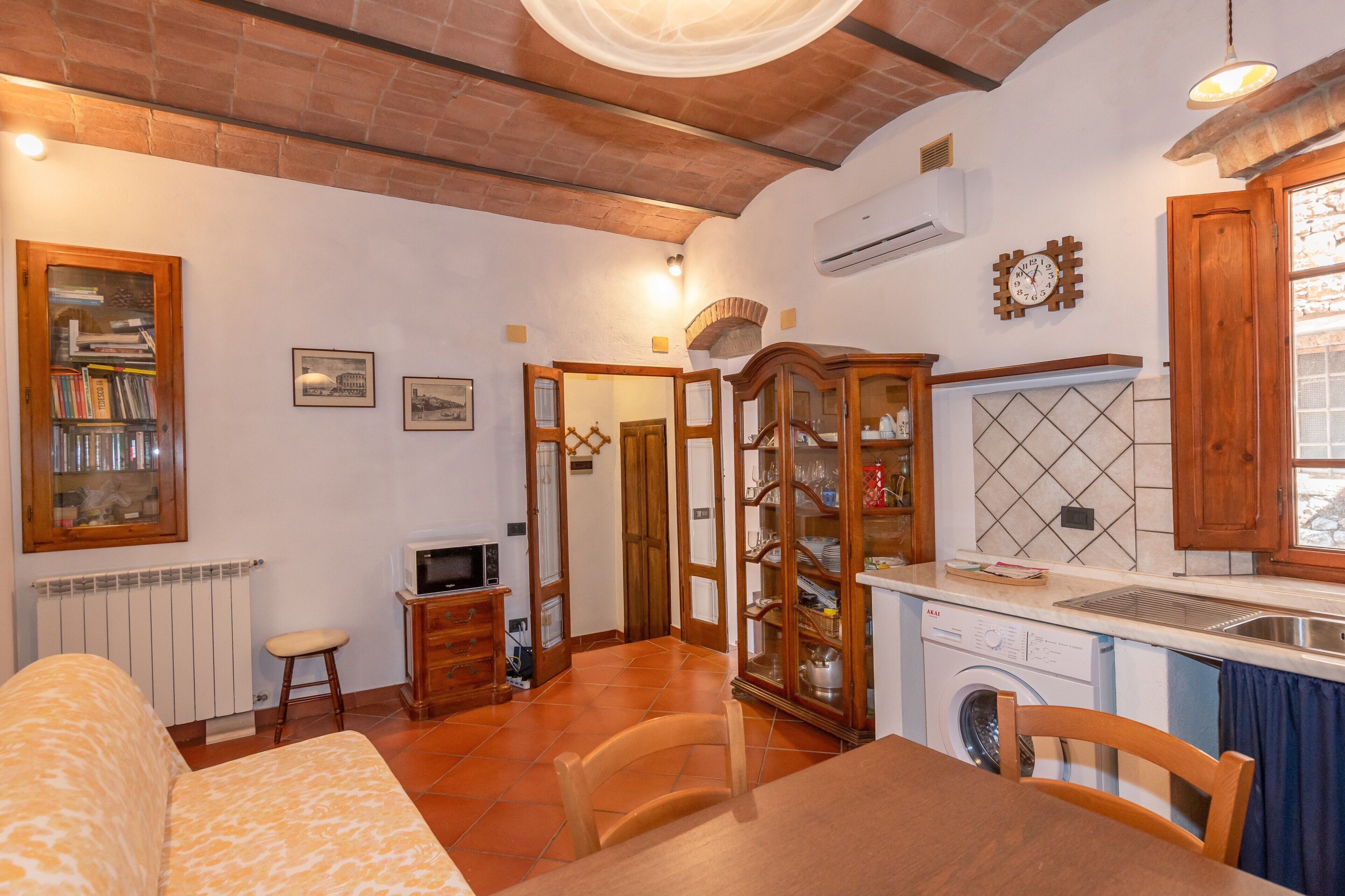 A compact living space with a sofa, dining table, kitchen area including a washing machine, and a small television.