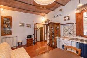 A compact living space with a sofa, dining table, kitchen area including a washing machine, and a small television.