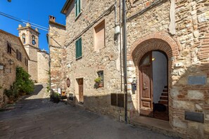 A narrow stone street with a building featuring an arched doorway and a bell tower.