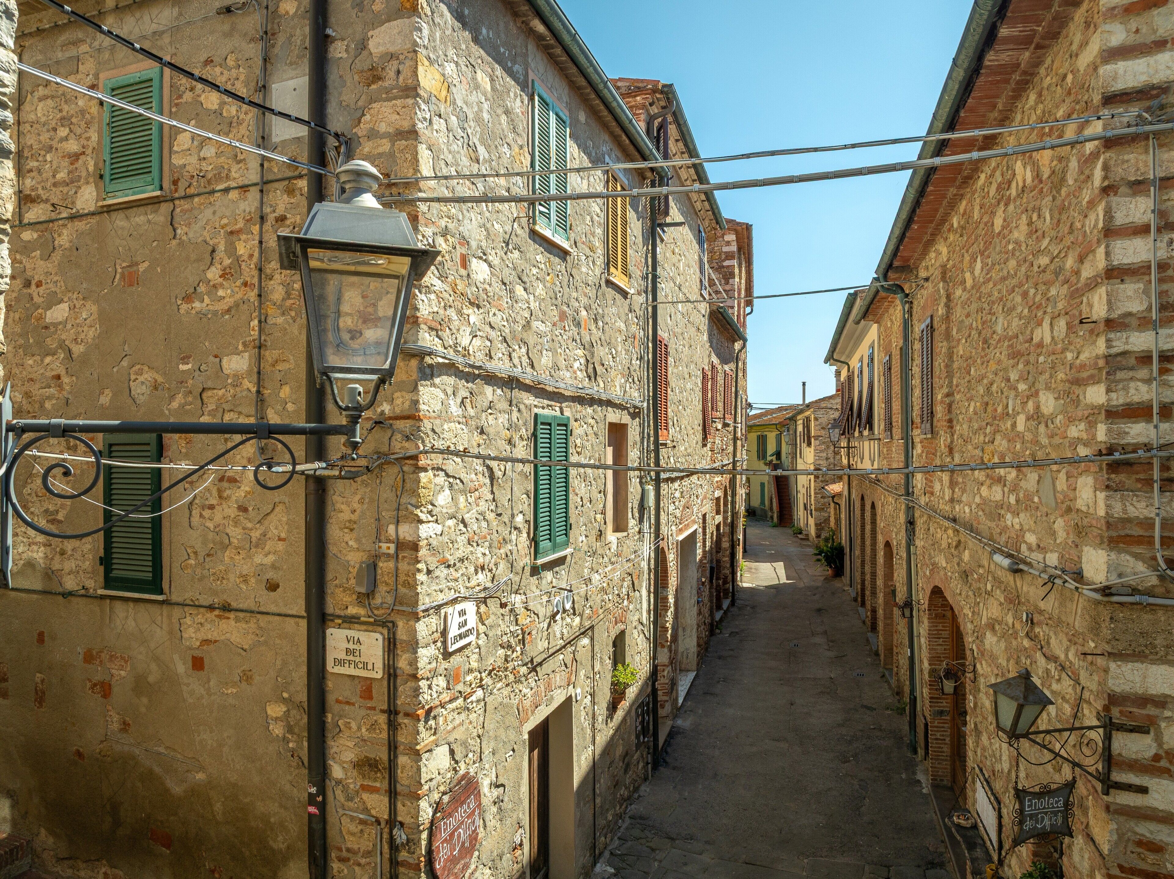 A narrow street with stone buildings, a street lamp, and signs indicating a local business.