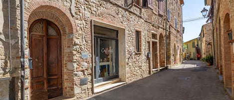 A narrow street with stone buildings, a wooden double door, and a shop with a large window.