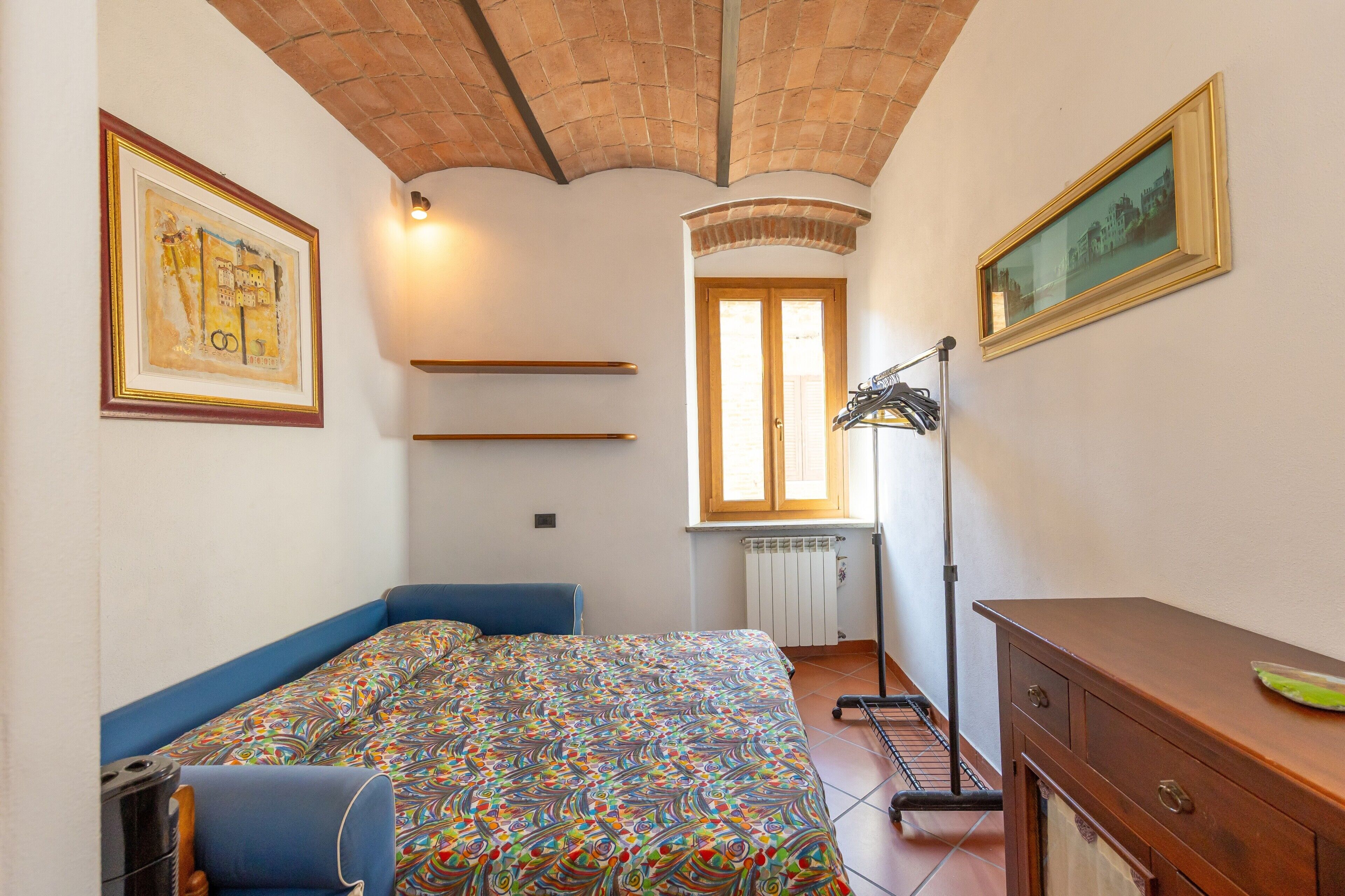 A bedroom with a bed, a dresser, a radiator, a window, and a door.
