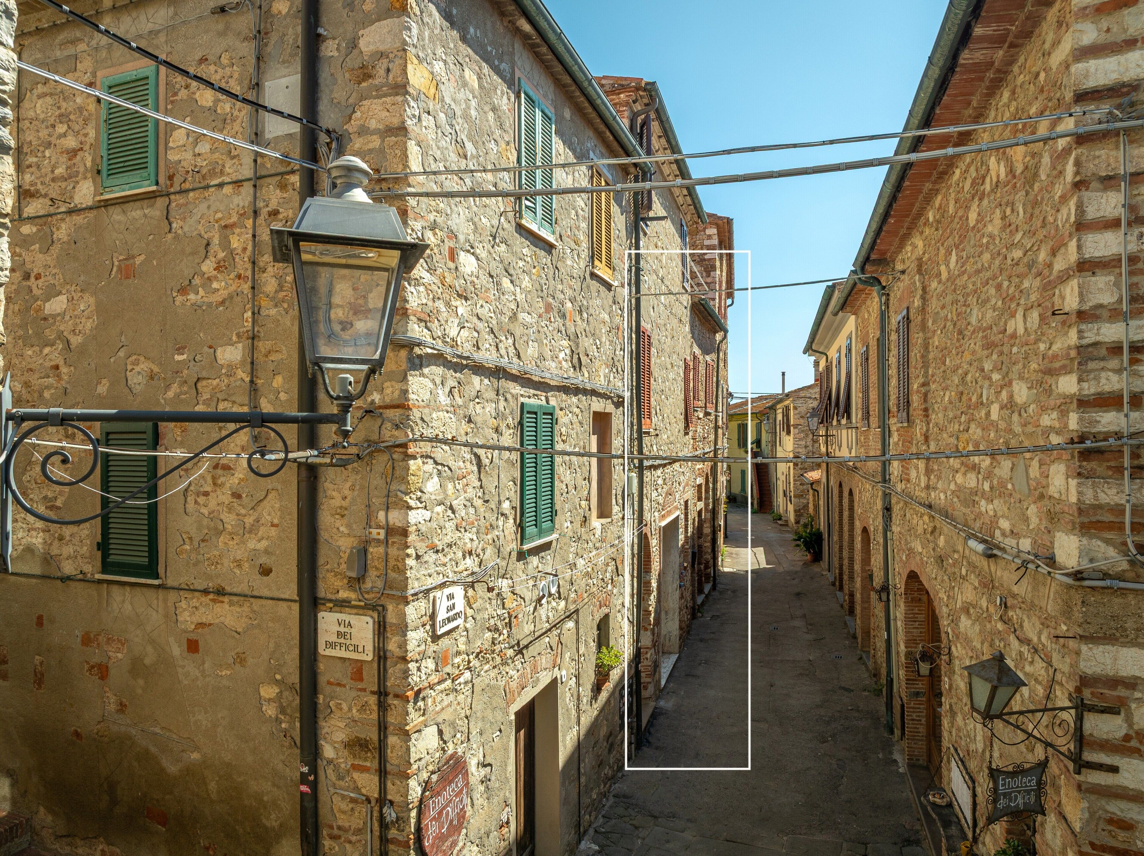A narrow street with stone buildings, a street lamp, and signs indicating a local business.