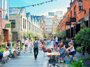 A bustling outdoor café with tables and chairs, surrounded by brick buildings and greenery. - Prime Chelsea Studio – 5 Min to Tube -Quiet & Safe (London)