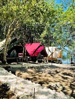 Un camping con varias tiendas de campaña, algunas con toldos rojos, ubicado cerca de una masa de agua.
