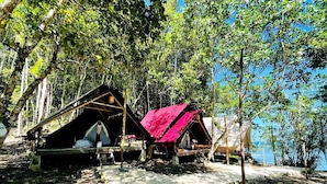 Un terrain de camping avec deux tentes, l’une avec un toit rouge et l’autre avec un toit noir, entouré d’arbres et sous un ciel dégagé.