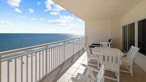 Un balcon avec vue sur l’océan, des meubles d’extérieur blancs et une porte vitrée.