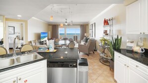 Une cuisine moderne équipée d’un lave-vaisselle, un coin repas avec une table et des chaises, et une vue sur l’océan.