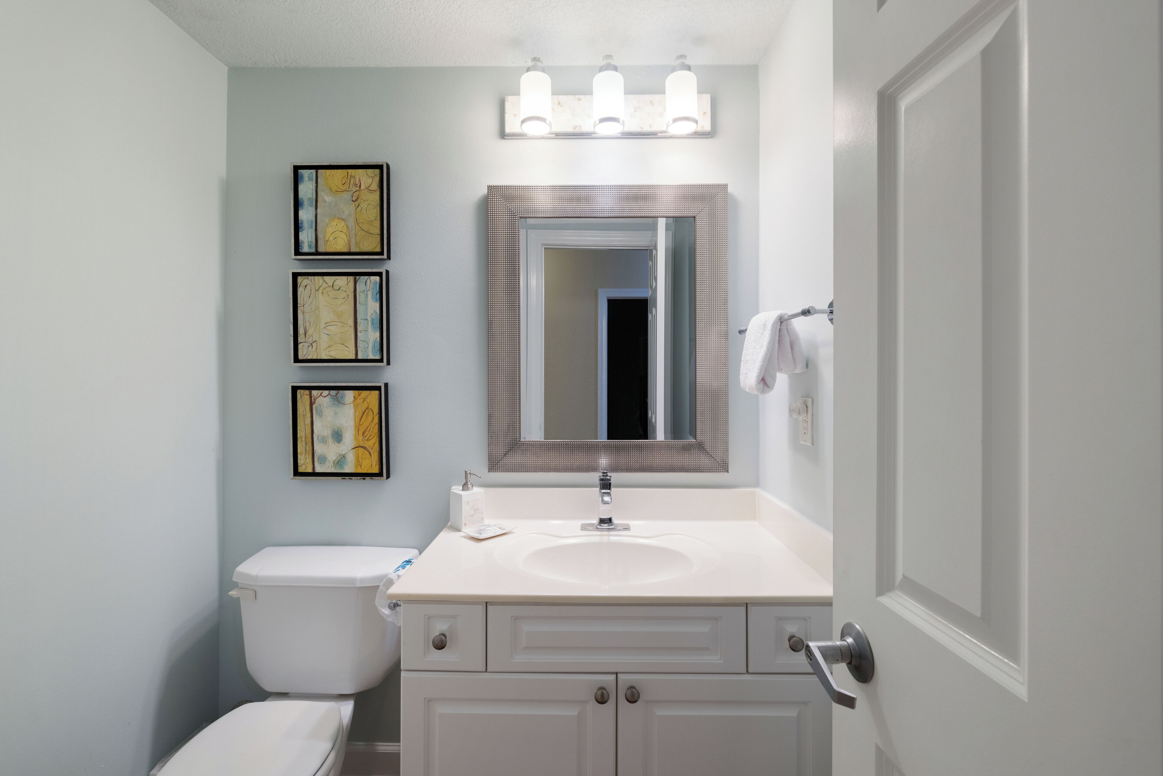 Une salle de bain avec des toilettes, un lavabo et un miroir. Trois tableaux encadrés sont accrochés au mur.