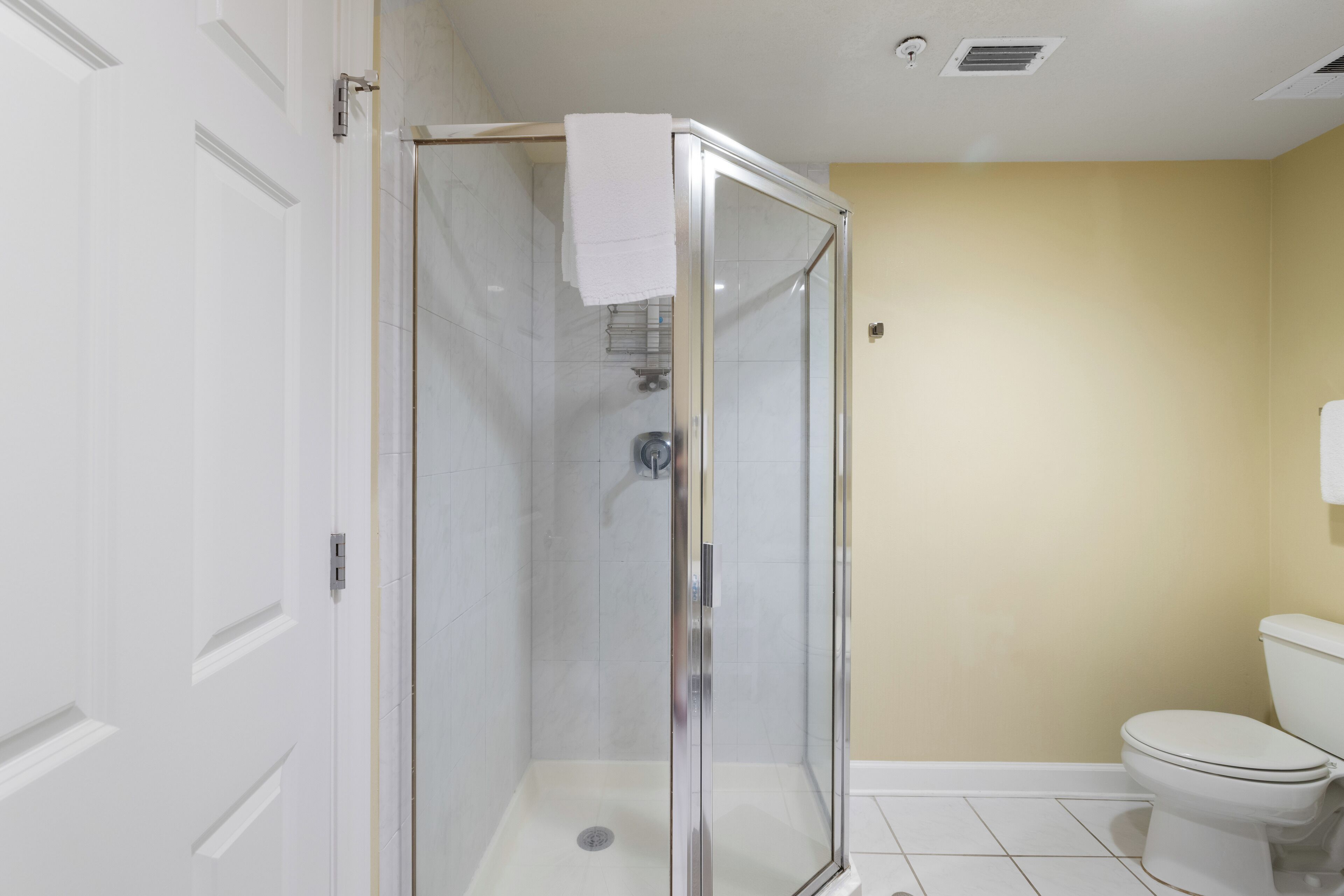 A bathroom with a glass-enclosed shower, white toilet, and beige walls.