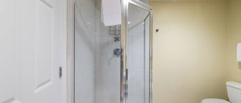 A bathroom with a glass-enclosed shower, white toilet, and beige walls.