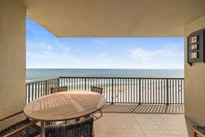 Un balcon avec une table et des chaises en bois, une vue sur la plage et une balustrade.