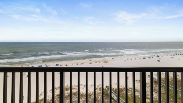 A beach view from a balcony with a railing, sandy beach, and ocean waves.
