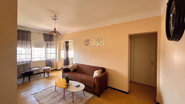 A living room with a brown sofa, a small coffee table, a rug, and a ceiling fan. - Apartment with sea view and Santa Cruz (Oran)