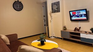 A living room with a brown sofa, a yellow coffee table, a clock, a television, and a plant. - Apartment with sea view and Santa Cruz (Oran)