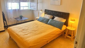 A bedroom with a bed, a nightstand, a lamp, a window with curtains, and a small table with a plant. - Apartment with sea view and Santa Cruz (Oran)