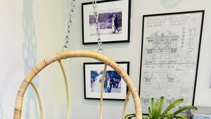 A room with a hanging chair, framed photographs on the wall, a plant, and a speaker on a wooden cabinet.