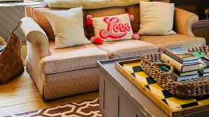 A cozy living room with a sofa, a coffee table with books, a woven basket, and a framed artwork on the wall.