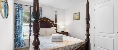 A four-poster bed with a floral bedspread, a bedside table with a lamp, and a large mirror on the wall.